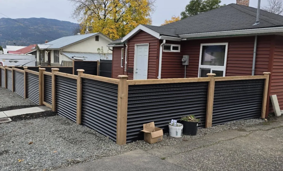 Black corrugated fence with natural cedar posts around a home