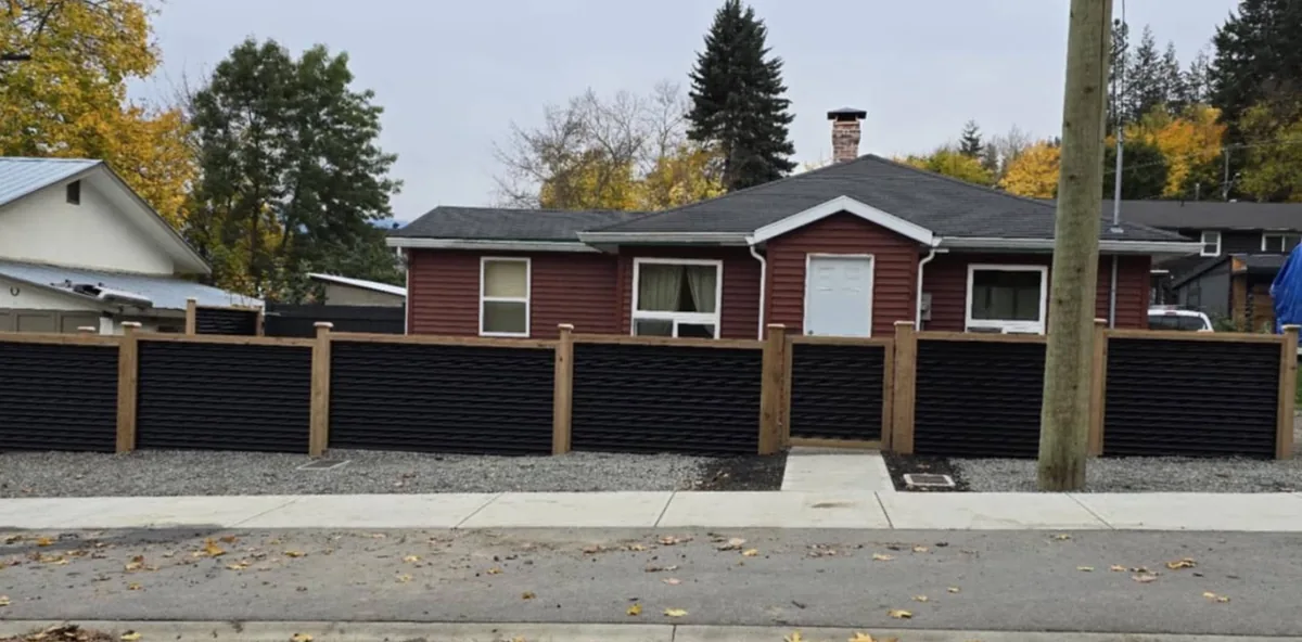 Black wave-pattern metal privacy fence framing a red house