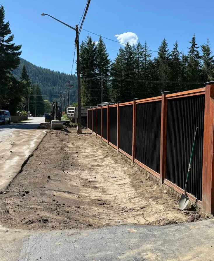 Black metal fence with warm stained-wood framing running along a rural road