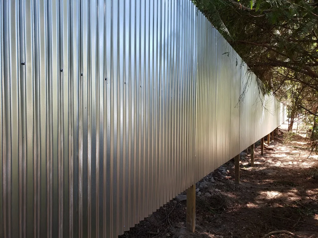 Galvanized metal fence panels running along a treeline