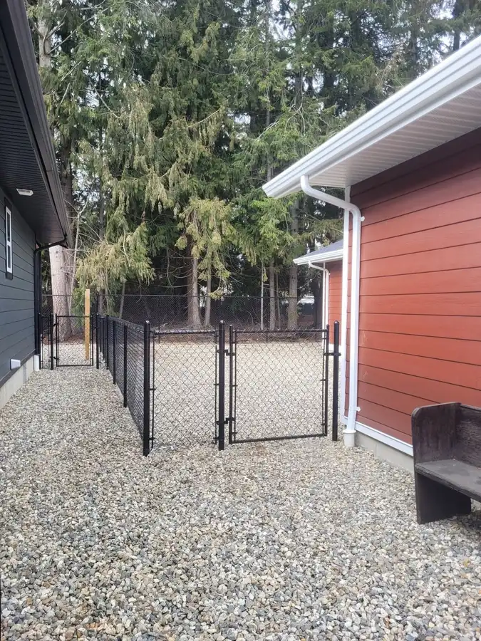 Black chain-link side-yard gate and fence line beside a red house