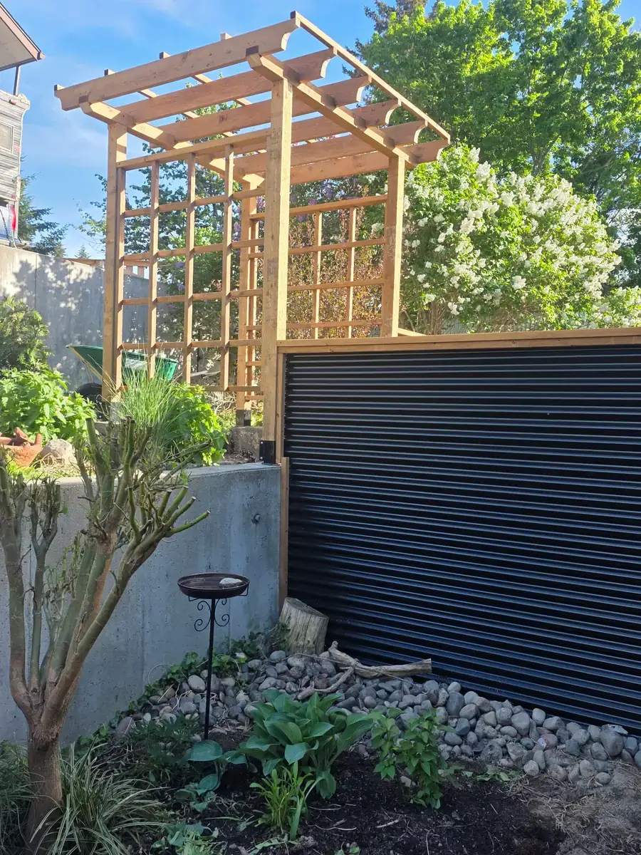 Cedar pergola and lattice screen above a black corrugated metal fence