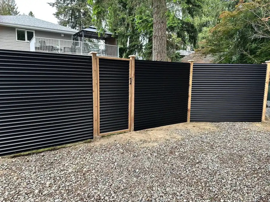 Black metal panel fence with a matching wood-framed gate along a residential driveway